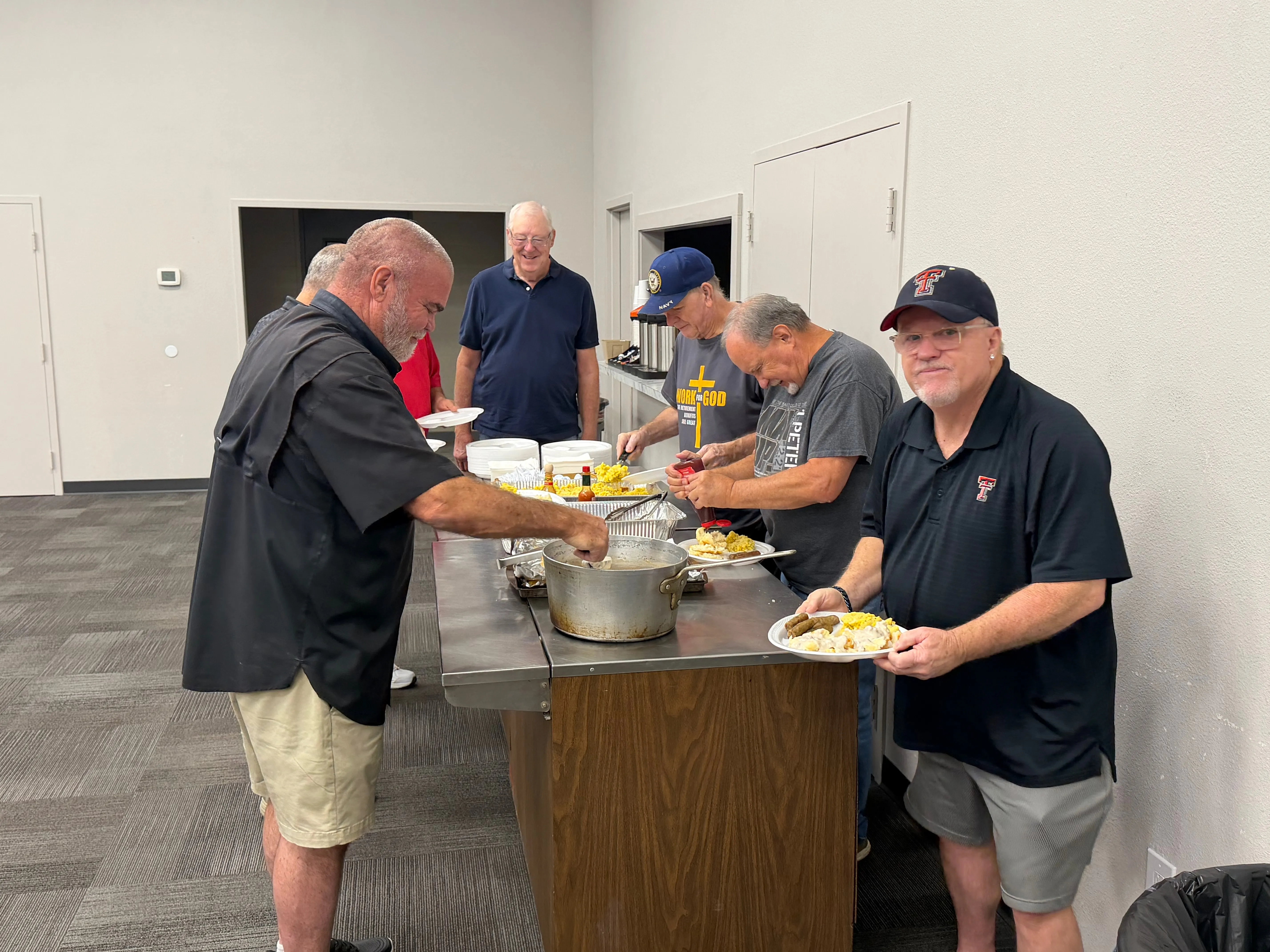 Men serving breakfast together at the food table